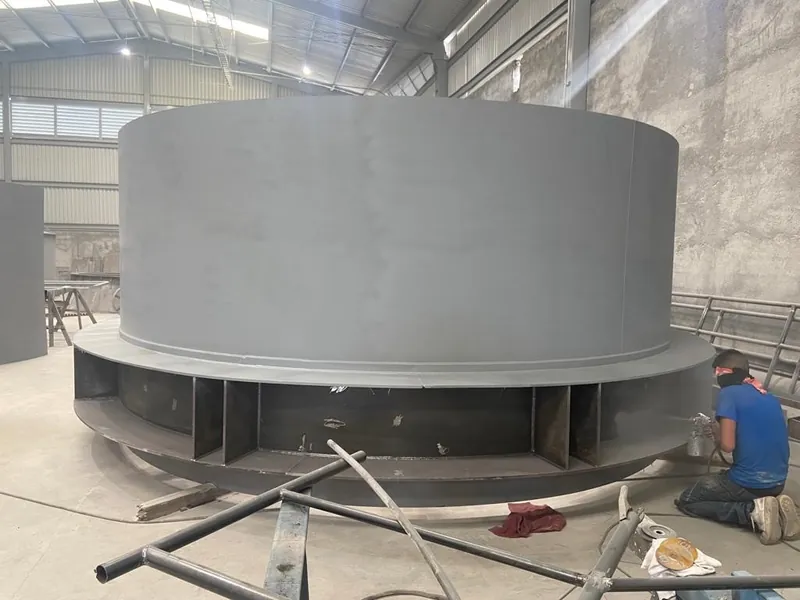 Tanque de acero de gran diámetro con un operario arrodillado al lado.